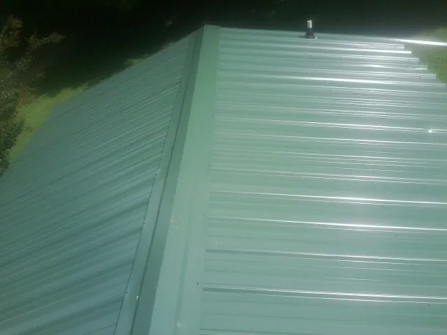 New green metal panels meeting at the ridge of a roof — Flat Roof Repair work by our crew in Westbrook
