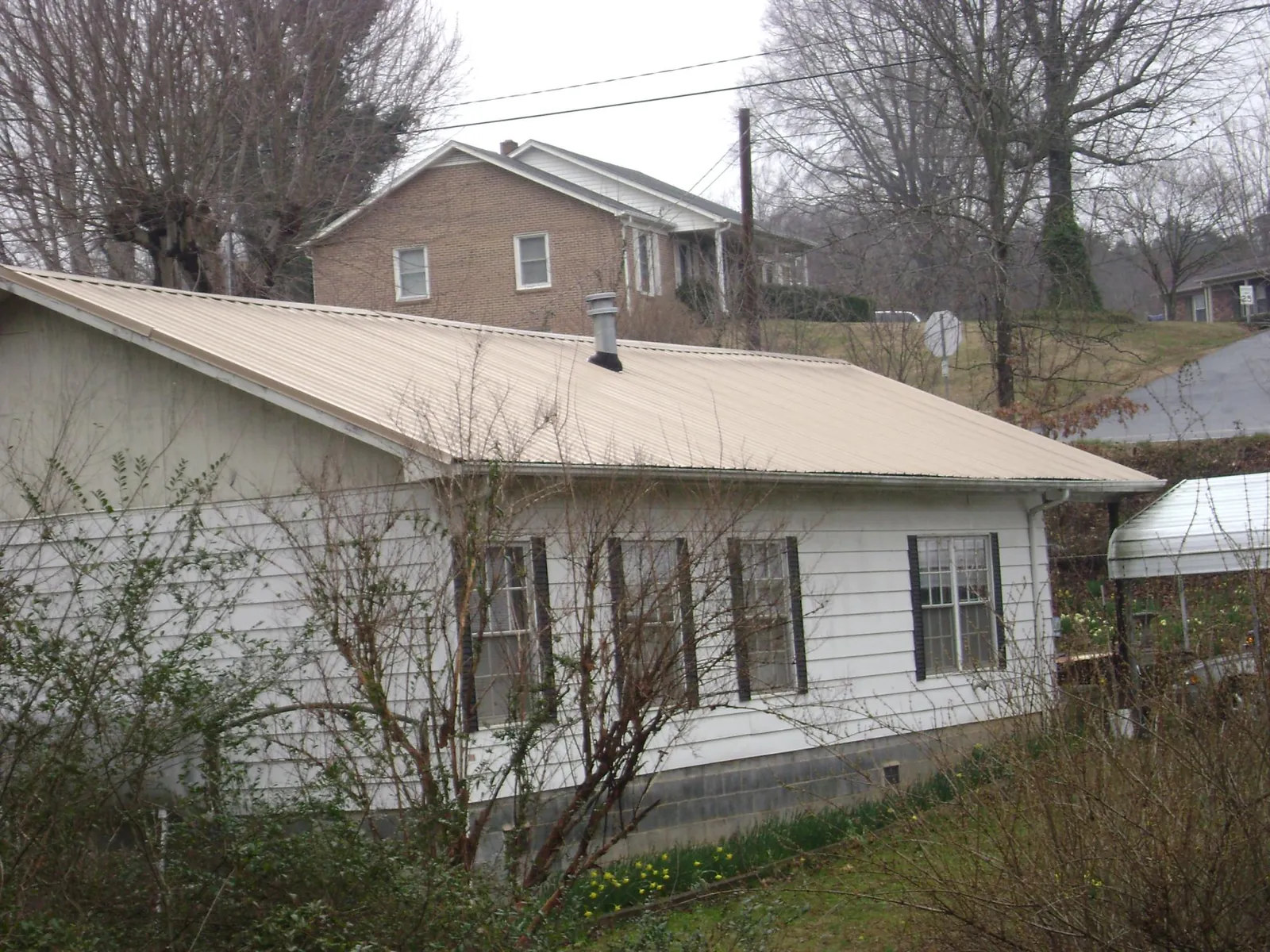 Tan metal roof on a white sided house set into a hillside — Commercial Roofing by Roofing Brothers in Westbrook